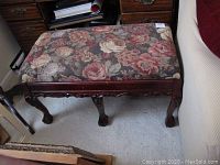 Top view of wooden bench with floral upholstered padded seat showing carved wooden legs and cherry finish.