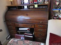 Full view of roll top desk showing roll top closed with wooden finish and eight drawers below.