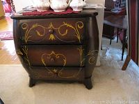 Front view of the chest of drawers showing three drawers with hand-painted floral and swirl designs in yellow paint against a dark cherry finish.