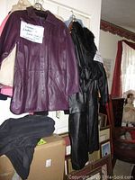 Purple leather coat hanging with other coats including black leather coat with fur collar and cream leather/suede jackets.