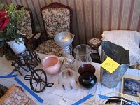 Overview of the lot on a table showing various vases including a metal bicycle vase stand with floral white vase, pink ceramic pot, dark amber and clear glass vases, and one cracked helmet-shaped birthday candle vase.
