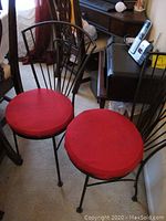 Two black metal chairs with red padded round seats next to wooden furniture in a room.