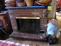 Faux brick electric fireplace with brass-colored metal framed black mesh screen and brass fireplace tools on the right side including the stand.