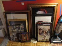 Photo of entire lot showing multiple framed artworks and plaques stacked against an orange wall beside a vacuum cleaner.