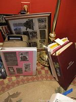 Photo shows Bell and Howell Autoload projector in hard case next to three binders filled with vintage movie pictures, standing on carpet next to a lamp.