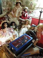 Seven dolls displayed on a chair and floor, showing porcelain heads and period clothing