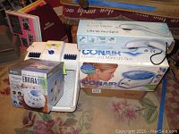 Photo displaying multiple personal spa and massage devices in their original packaging including Dr. Scholl's luxury foot spa, Homedics Enviraspa, Conair Paraffin spa, and others.