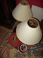 Two beige pleated lamp shades on top of one another with several other lamp shades nearby.