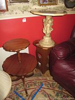 Three side tables are shown: a large octagonal faux marble top pedestal table with cream cherub sculpture base, a dark wood two-tier scalloped edge table, and a smaller reddish brown heart-shaped painted wooden table with cutout shapes.