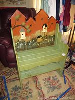 Front view of painted wooden bench showing green seat and sides with birdhouse mural backrest.