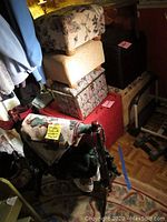 Photo shows wooden quilt rack with multiple blankets including Afghan, various upholstered stools, and a floral-patterned storage ottoman.