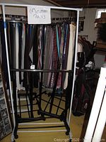 Photo showing black metal and white plastic clothes racks with caster wheels, with garments hanging on a rack in the background not included.