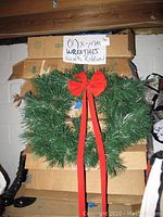 One green artificial Christmas wreath with a red bow hanging in front of cardboard boxes.