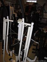 Folded view of the XL glider exercise machine showing the white metal frame, black footpads, handles, and cables.