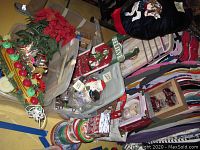 Wide view showing Christmas carousel horse tree skirt alongside fake poinsettia flowers, assorted tins, decorative sled, candles, and plastic bins.