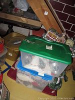 Several plastic storage bins stacked with lids in green, blue, yellow, and red containing Christmas village items and accessories.