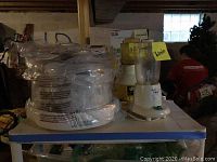 Photo of the lot placed on a surface showing stacked kitchen appliances with plastic wrap and labels indicating items