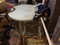 Photo showing white round plastic patio table with textured surface, folded blue and white striped umbrella, and glass top metal side table