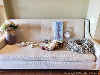 View of all 10 items including clock, wreath, wall art, silver pieces, and floral figurines laid on beige sofa.