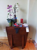 Wood cabinet with various items on top including faux floral arrangements, linens, and candle