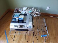 Brother MFC440CN multi-function printer/copier/scanner with cables, manuals, and two metal wire stands on hardwood floor.