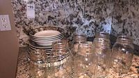 Photo showing stacked decorative plates with geometric and swirl patterns and clear glass jars with metal lids on granite countertop.