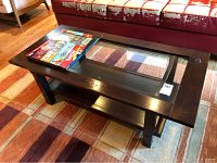 Wood and glass coffee table with visible stains and scratches on wood surface, glass tabletop intact. Board games laid on table surface.