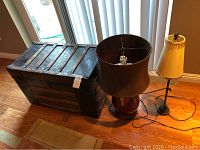Photo showing vintage steamer trunk and two table lamps placed on wooden floor near window.