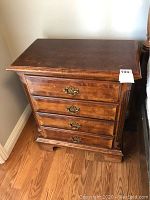 Front view of wooden nightstand showing four drawers with decorative metal handles and overall condition.
