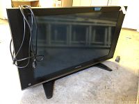 Full view of Panasonic flat screen TV showing black bezel, screen, and attached power cord, standing on floor.