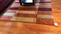 A section of the area rug showing the geometric block pattern with earth tone colors and wood flooring underneath.