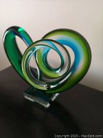 Front three-quarter view of green and blue glass spiral sculpture on clear pedestal