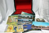 Photo of multiple vintage postcards fanned out in front of open wooden jewelry box with red interior.
