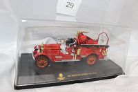 Side angle view of the red 1921 American LaFrance fire truck die cast model with gold and black detailing inside clear display case on black base.