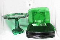 Green vintage glass pedestal cake display plate next to 6 matching square plates