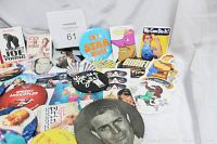 Multiple assorted buttons, pins, and magnets arranged on white background showing different themes and sizes including movie stars and pop culture icons