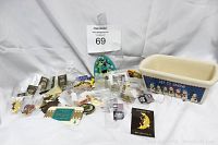 Overview photo showing multiple assorted memorabilia pins in plastic bags alongside a blue and white ceramic container with 'Let It Snow' and snowmen artwork