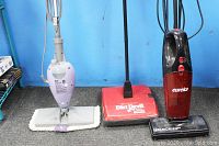 Lot of three floor cleaners: Shark floor steamer (left, white/gray), Dirt Devil handheld vacuum (center, red/black), Eureka upright sweeper vacuum (right, red/black)
