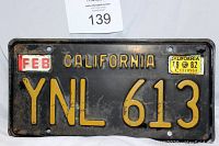 Front view of vintage black California license plate from 1982 with yellow embossed characters YNL 613, FEB month sticker, and 1982 registration decal