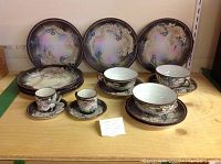 Full set of Japanese Moriage dragonware showing plates, teacups and saucers with dragon motifs and iridescent coloration.