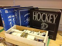 Photo of three sports card albums: two hockey card albums (blue and black) and one blue baseball card album, along with a white cardboard box filled with loose baseball cards and packs.