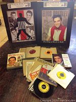 Two Elvis Presley metal collector signs displayed upright with a collection of vintage 45 rpm vinyl records in front.