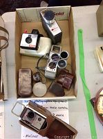 Overview of cameras and accessories in box with notes about vintage photographic equipment.