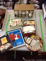 Wide view of the table showing the plastic drawer organizer with stamps, multiple boxes filled with stamps, round tin, and two albums