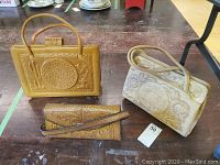 Three different tooled leather purses on a table: two handbags with double handles and one clutch with latch closure.