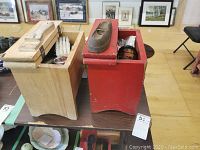 Two wooden shoe shine kits, one natural wood, one red painted, placed on a table showing exterior and some contents.
