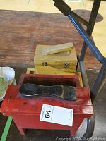 Red wooden shoeshine kit box with black shoe rest on top, showing signs of use.