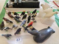 Overview of approximately 25 assorted bird figurines, showing two large white birds on square bases and numerous smaller detailed bird figurines in various colors.