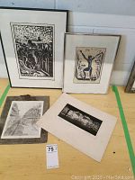 Four black and white prints arranged on a table including two larger framed pieces and two smaller prints, one mounted on stone slab