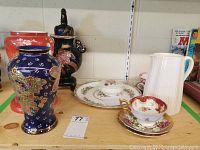 Photo showing Coalport china including white pitcher, decorative plates, teacups with saucers, and three vases of differing colors and designs.